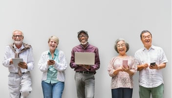 Diverse group of senior people in a line, smiling and using tech devices such as laptops and tablets