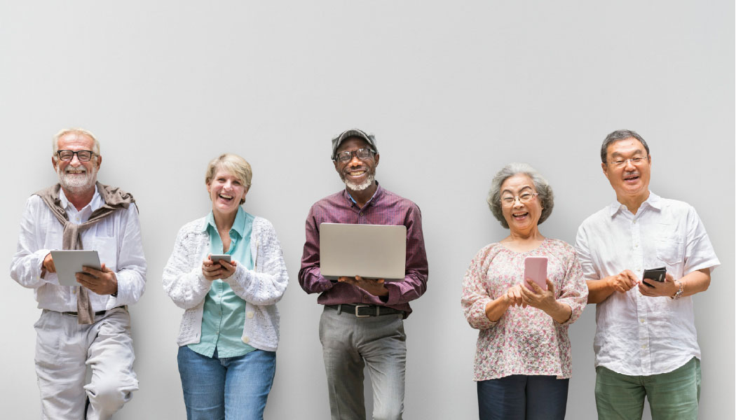 Diverse group of senior people in a line, smiling and using tech devices such as laptops and tablets